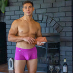 Man in pink underwear holding a wooden object in front of a brick wall.